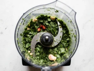 Fresh ingredients for Easy Zhoug Sauce arranged on a wooden table: cilantro, garlic, green chilies, olive oil, lemon, and spices.