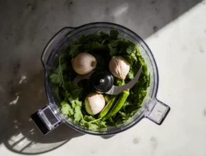 A bowl of vibrant green Easy Zhoug Sauce with olive oil drizzle and pita bread, a fresh Middle Eastern condiment made with cilantro and chili.