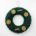 Finished green fabric wreath of forest-green petals with dried orange slices, cinnamon sticks and red berries