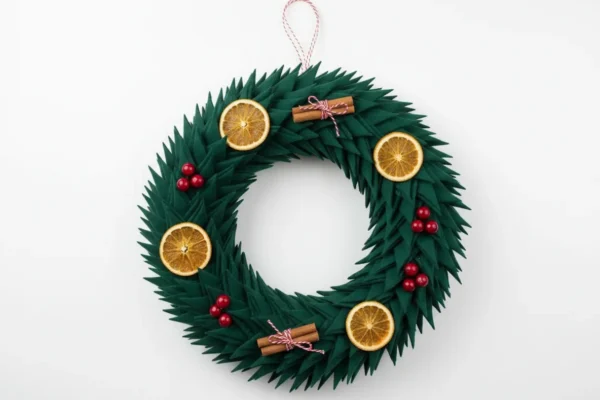 Finished green fabric wreath of forest-green petals with dried orange slices, cinnamon sticks and red berries